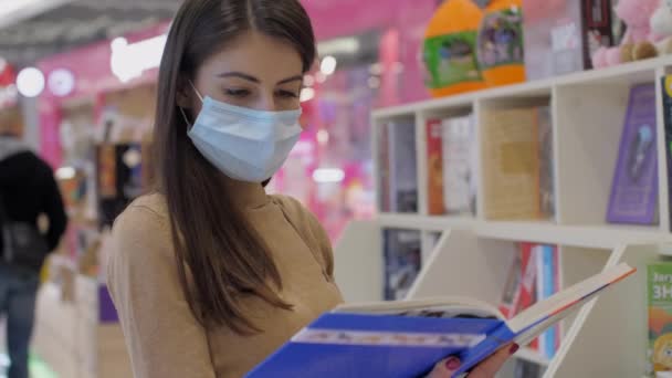 Νεαρή γυναίκα με μάσκα προσώπου μιας χρήσης εξετάζει το βιβλίο — Αρχείο Βίντεο