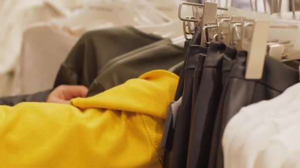 Ung kvinna i ansiktsmask tittar på kläder på hängare — Stockvideo