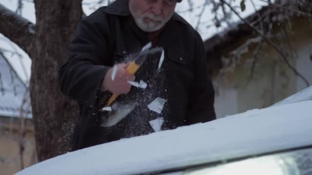 Homem envelhecido limpa capuz de automóvel da neve com raspador de gelo — Vídeo de Stock