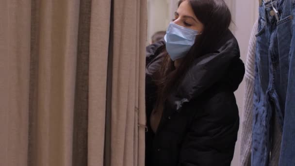 Lady in disposable mask puts winter coat off in fitting room — Stock Video