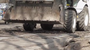 Bozuk yol boyunca metal kepçeli büyük traktör.