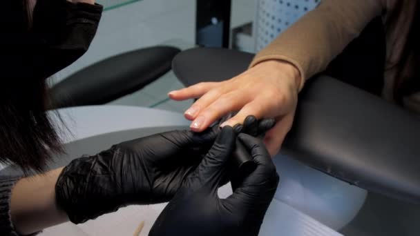 Косметолог наносить кольоровий гель на нігті молодої жінки — стокове відео