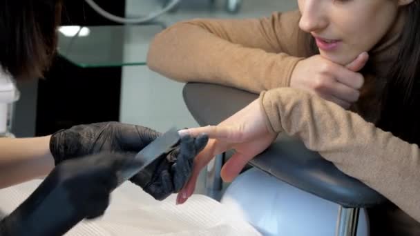 Jonge vrouw glimlacht en kijkt naar manicure in salon — Stockvideo