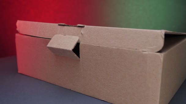 Brązowe pudełko papierowe leży na stole przed zieloną i czerwoną ścianą — Wideo stockowe