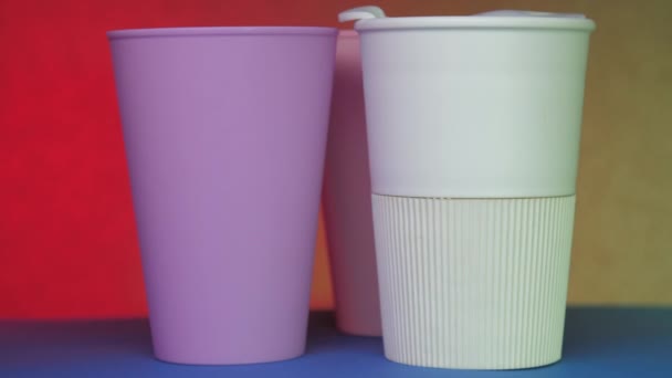 Purple white and pink beverage cups rotate on blue table — Stock Video