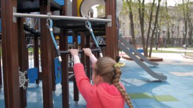 Uzun örgülü liseli kız metal salıncakta sallanıyor.