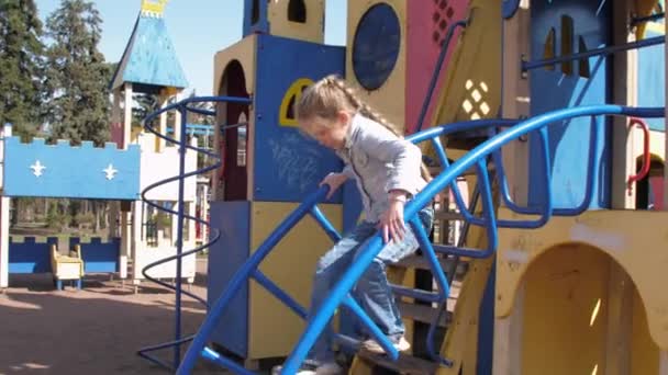 Junior schoolgirl in pullover climbs up metal attraction — Stock Video