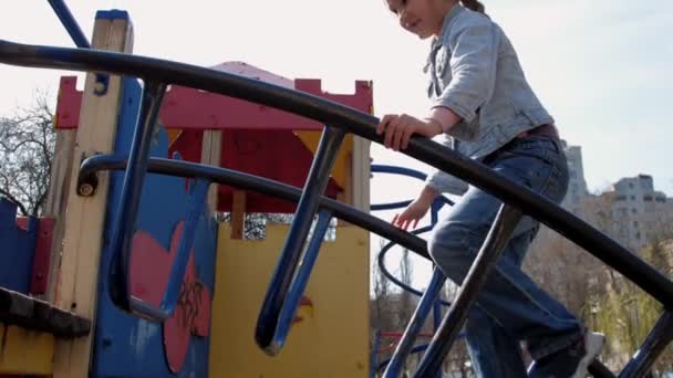 Junior schoolgirl in pullover climbs up metal attraction — Stock Video