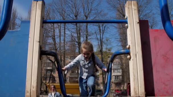 Junior schoolmeisje in pullover klimt omhoog metalen attractie — Stockvideo