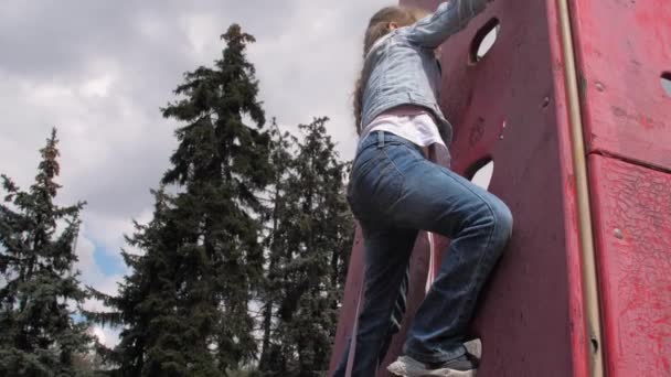 Blond junior schoolmeisje met vlecht klimt omhoog houten muur — Stockvideo