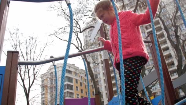 Wanita muda ketakutan melangkah di jembatan gantung di taman bermain — Stok Video