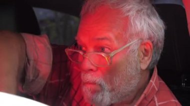 Sakallı ve gözlüklü sarhoş adam arabada oturuyor.