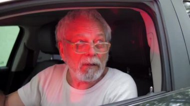 Yaşlı adam, yanıp sönen ışıkların altında ciddi bir yüzle konuşuyor.