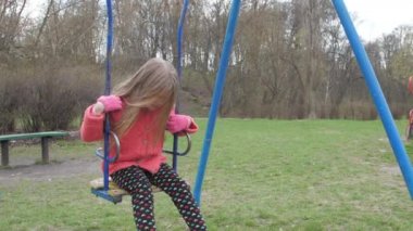 Uzun sarı saçlı üzgün liseli kız mavi salıncakta oturuyor.