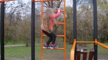 Uzun sarı saçlı liseli kız metal merdivenlere tırmanıyor.