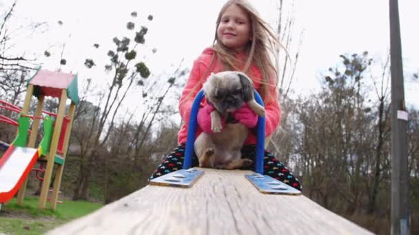 Junior écolière blonde s'assoit sur l'attraction et tient chien — Video