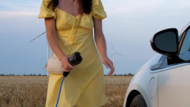 EV laddas av vindkraftverk kvinna sätter plugg till auto — Stockvideo