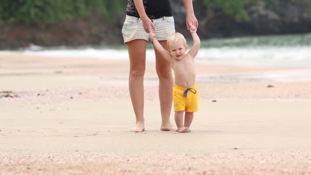 Child walks by handle with mother on beach — Stock Video