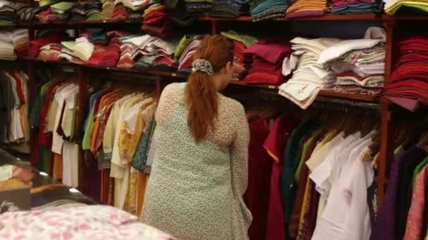 Mujer elige ropa en una tienda — Vídeo de stock