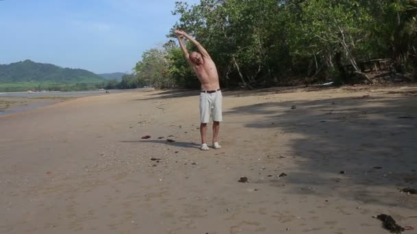 Stary człowiek robi jogi na plaży — Wideo stockowe