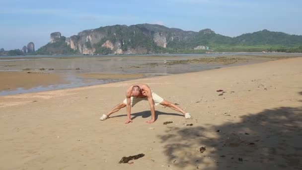Oude man doet yoga op het strand — Stockvideo