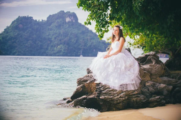 Невеста сидит на скале на пляже — стоковое фото