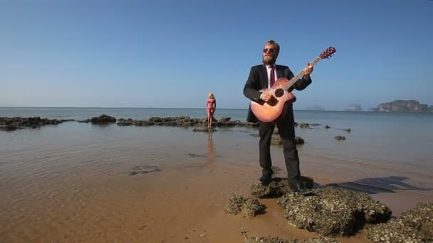 Гітарист грає для дівчинки біля моря — стокове відео