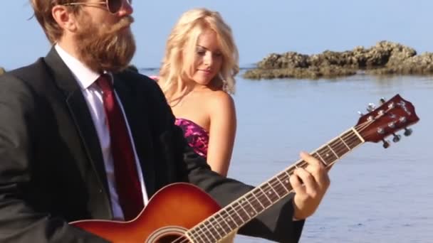 Девушка и мужчина с гитарой на пляже — стоковое видео