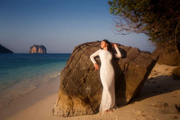 Bruid leunt op grote rots op strand — Stockfoto