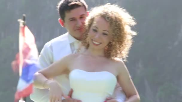 Bruidegom knuffels bruid tegen flappen vlag — Stockvideo
