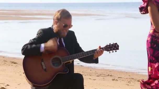 Gitarist toneelstukken en meisje dansen op strand — Stockvideo