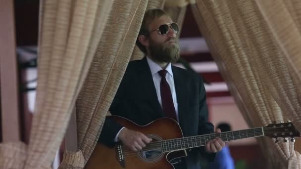 L'uomo barbuto in abito nero suona la chitarra — Video Stock