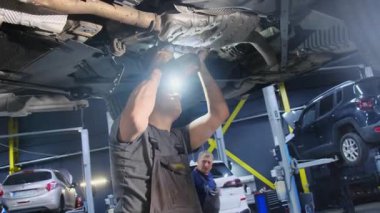 Uzman bir tamirci kaldırılmış arabanın şasisine vida takıyor. Benzin istasyonunda tornavidayla çalışan adam otomobil tamir ediyor.