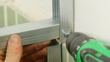 İşçi, elektrikli tornavidayı kullanarak metal panelleri vidayla kapatıyor. Tamirci banyoya alçıdan duvar yapmak için inşaat yapıyor.