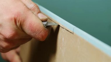Adam atölyede alçı paneli küçük bir bıçakla dikkatlice kesiyor. Tamirci daha fazla iş için gerekli malzeme boyutunu yaratıyor