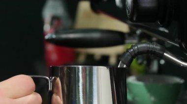 Barista espresso makinesinin altında süt köpürten sürahi pozisyonunda. Kadın işçi, kahve için köpüren sütü buharlı çubuğun altında tutuyor.