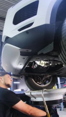 Tamirci, konserve kutusundan maddeyi arabanın altına püskürtür. Usta, araba tamirhanesinde duran aracın yüzeyini tozdan temizliyor.