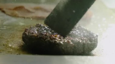 Aşçı, cızırdayan köfteyi metal spatulayla dikkatlice ayarlar. Şef kaynamış yağın üzerinde hamburgerleri kızartıyordu. Yavaş çekim