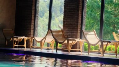 Rahat ahşap iskemleler kapalı yüzme havuzunun kenarında duruyor. Yüzmek ve lüks kaplıcalarda dinlenmek için sakin bir yer.