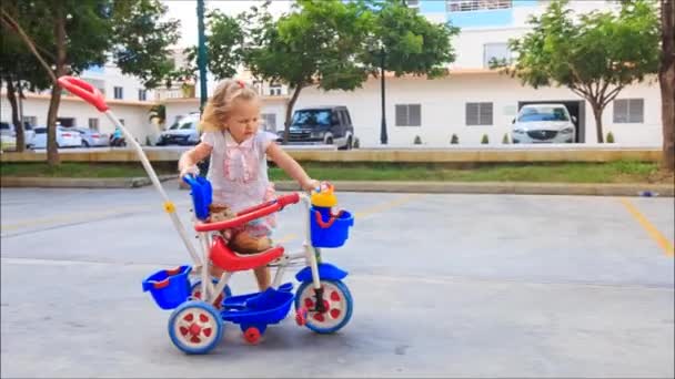 Menina empurra criança do carrinho triciclo — Vídeo de Stock