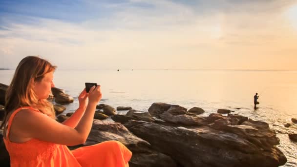 Mulher tirando fotos da costa do pôr do sol — Vídeo de Stock