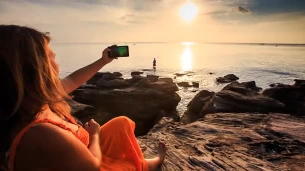 Mulher tirando fotos da costa do pôr do sol — Vídeo de Stock