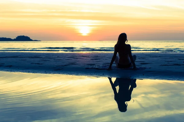 Menina sentada na praia do mar ao pôr do sol . — Fotografia de Stock