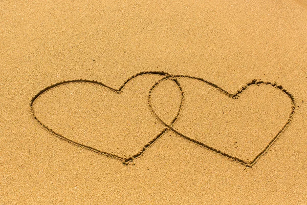 Två intrasslade hjärtan på sandstrand. — Stockfoto