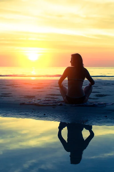 Silhouet jonge gezonde vrouw het beoefenen van yoga op het strand bij zonsondergang. — Stockfoto