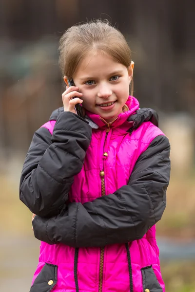 Porträt eines kleinen süßen Mädchens, das auf dem Handy im Freien spricht. — Stockfoto