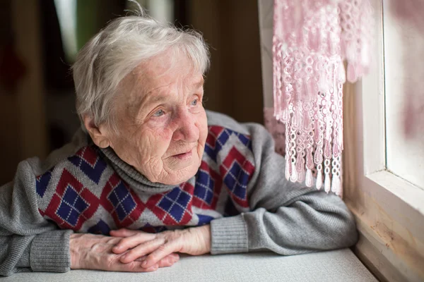 Äldre kvinna tittar ut genom fönstret — Stockfoto