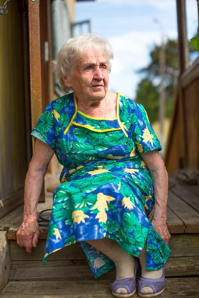 Old woman sitting on the porch — Stock fotografie