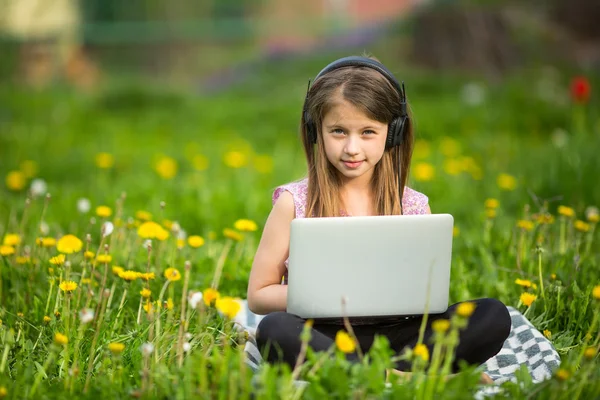 Petite fille dans les écouteurs avec ordinateur portable — Photo