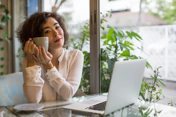 Asian woman with coffee cup and laptop — Stock Photo, Image